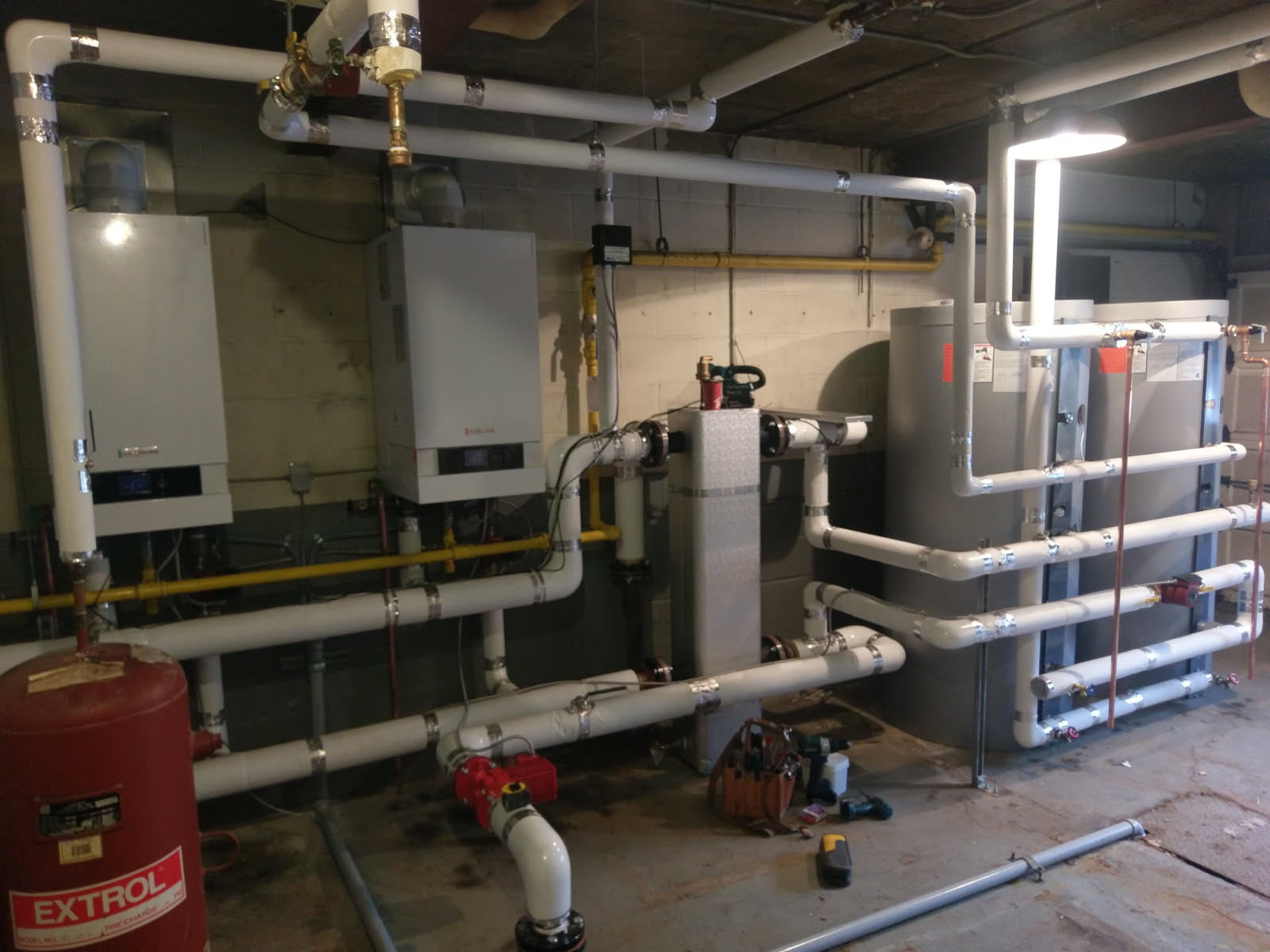 Two wall-hung boilers with insulated white piping, an Extrol expansion tank and buffer tanks in a commercial plant room