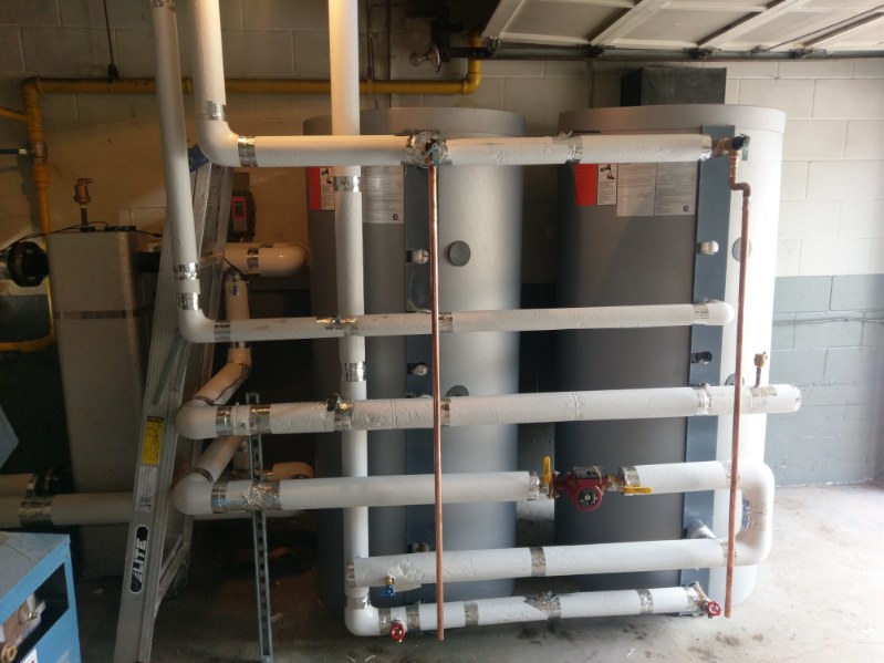 Two buffer tanks with insulated white piping and circulator pumps in a mechanical room