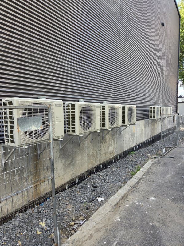 A row of ductless outdoor units mounted on brackets along the side of a large building