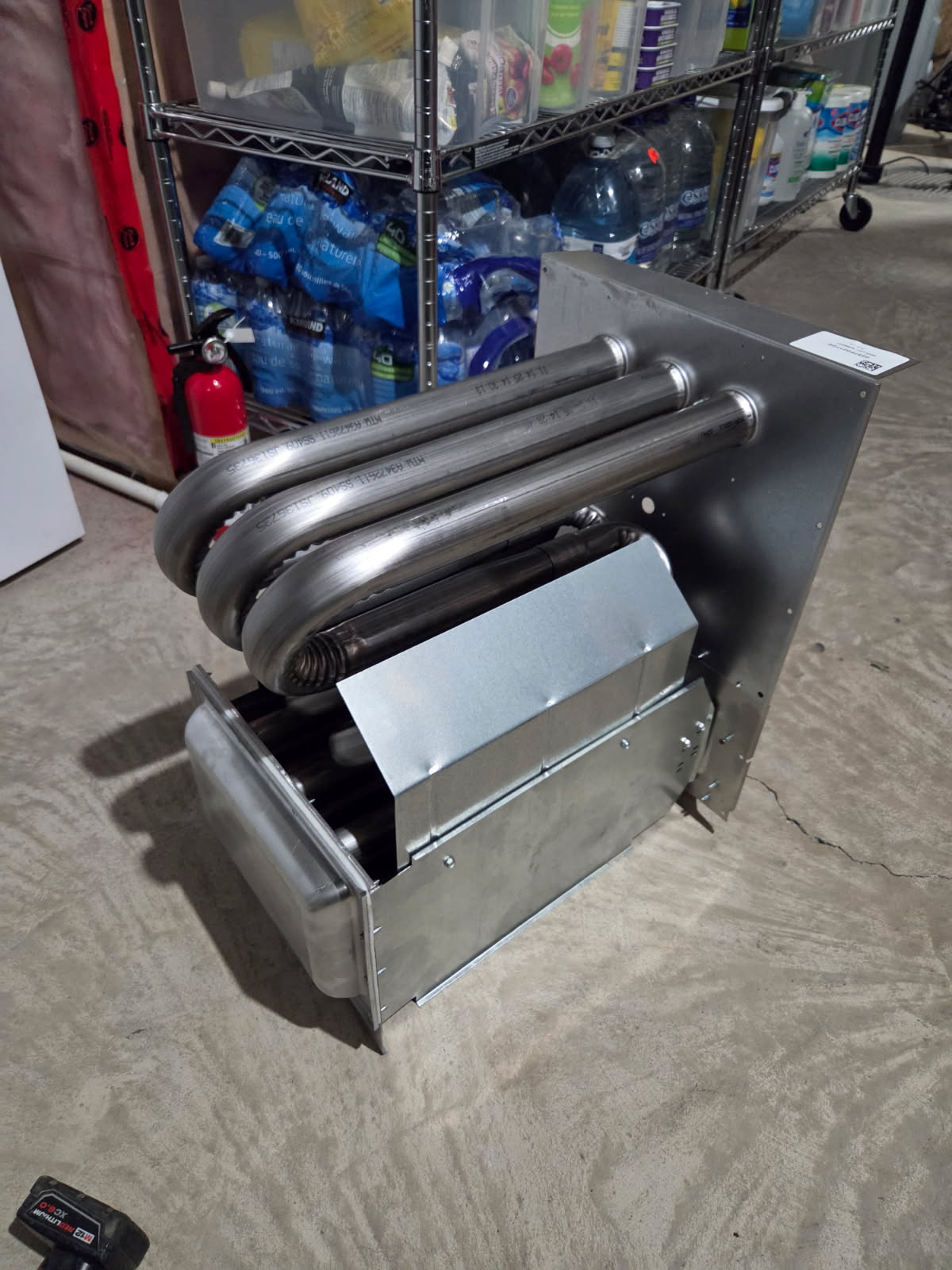 A new stainless steel furnace heat exchanger with three return bends sitting on a basement floor