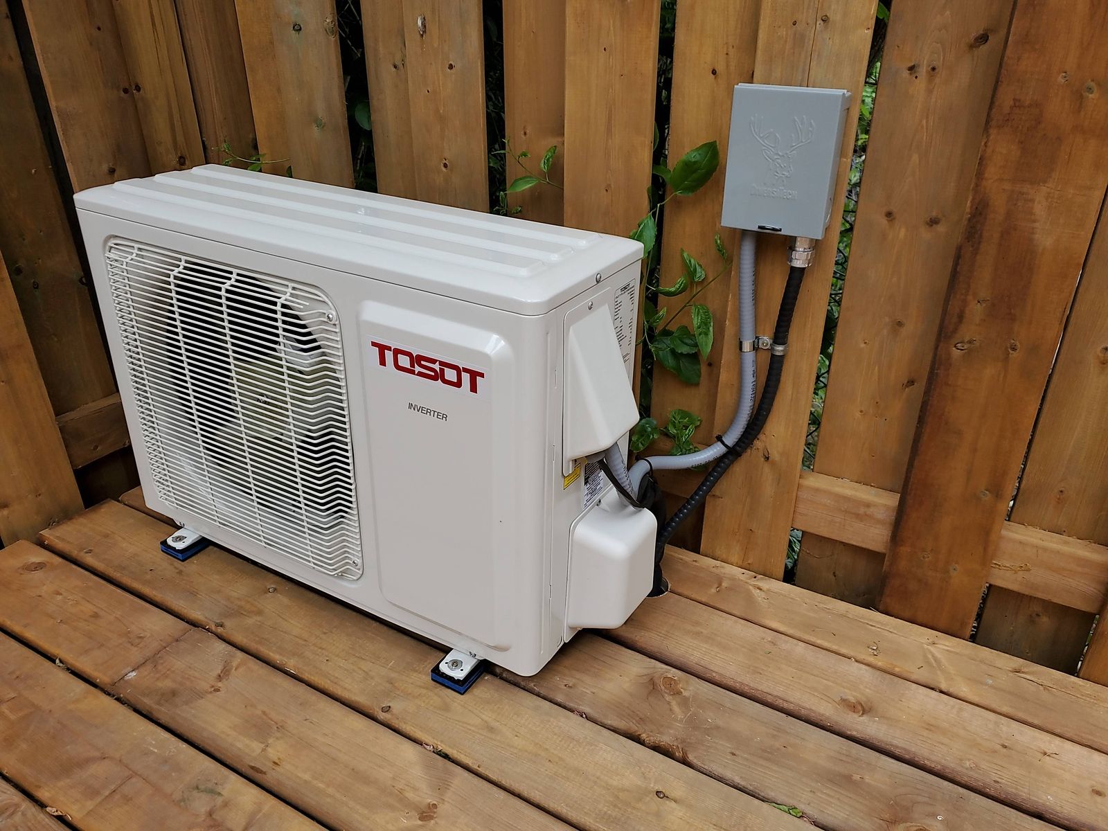 A white ductless heat pump outdoor unit on a wooden deck beside a fence