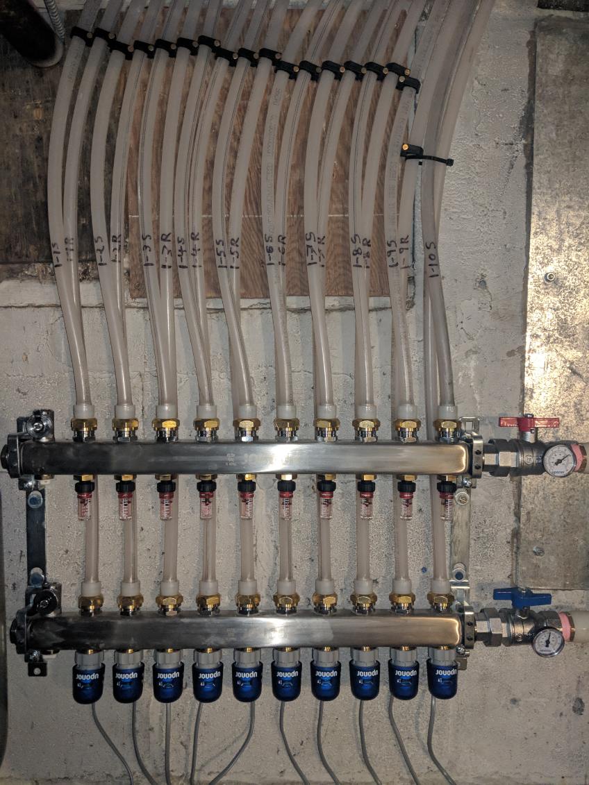 A stainless in-floor heating manifold with ten labelled PEX loops, flow meters and zone actuators